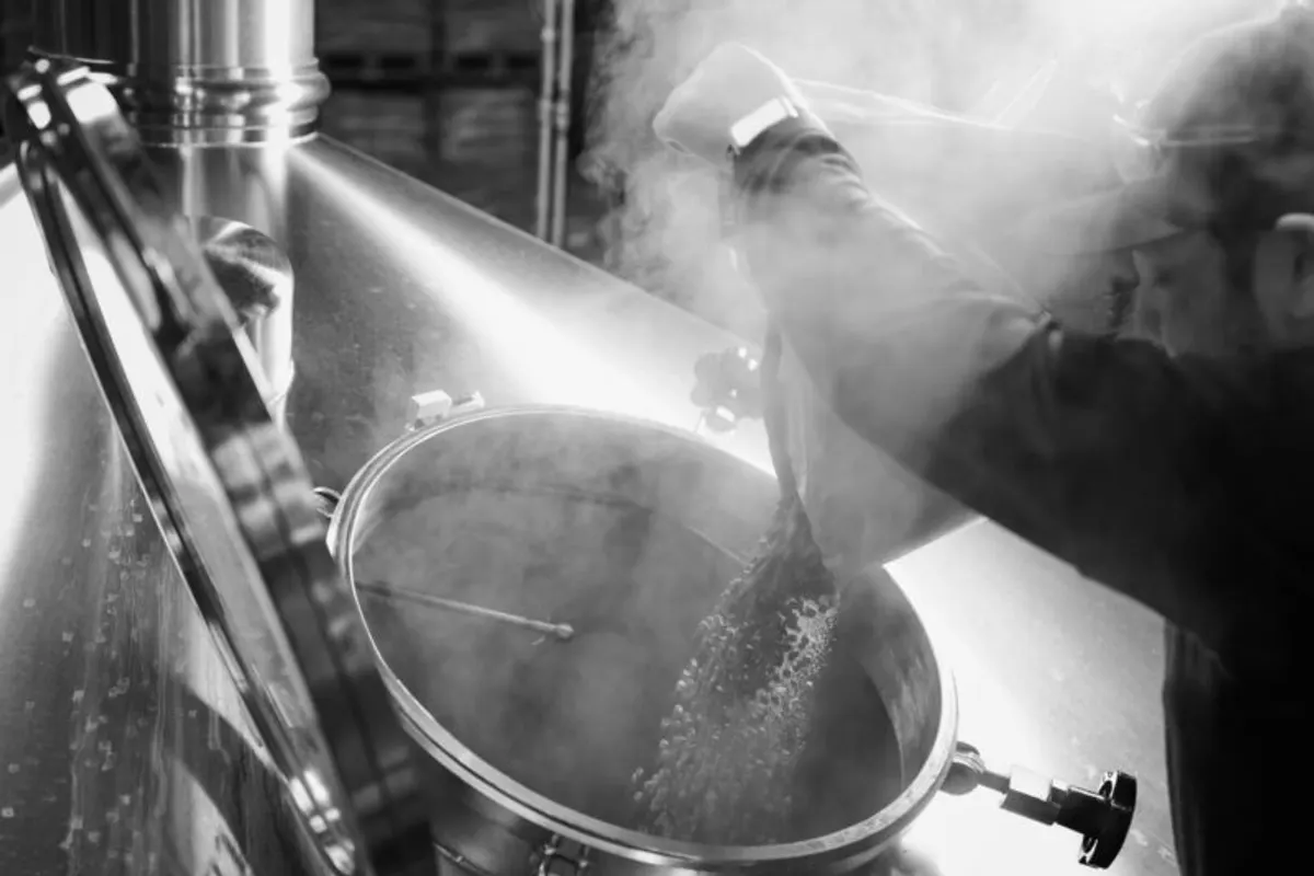 Brewer stirs a steaming kettle at the brewery