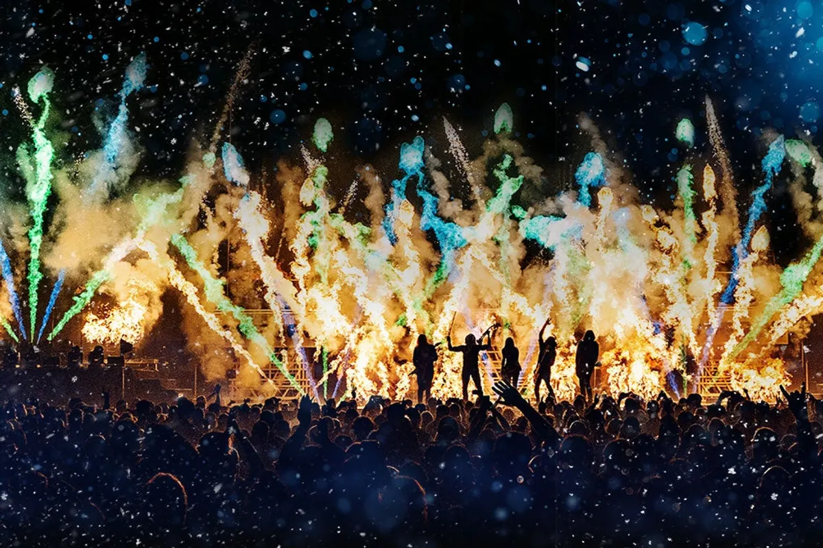 Band silhouetted on stage before a crowd, with flames and pyrotechnics