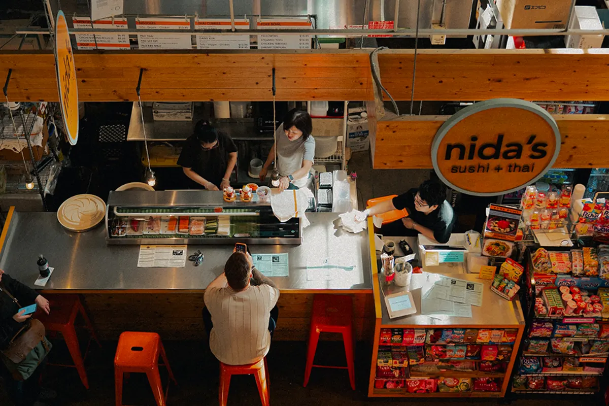 Overhead view of vendors and diners at Nida's sushi counter in the market
