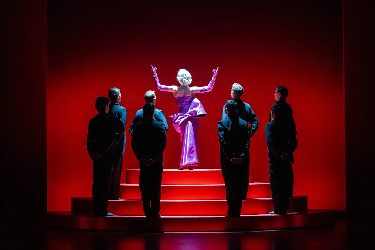 Dancer in a purple gown atop red steps surrounded by men