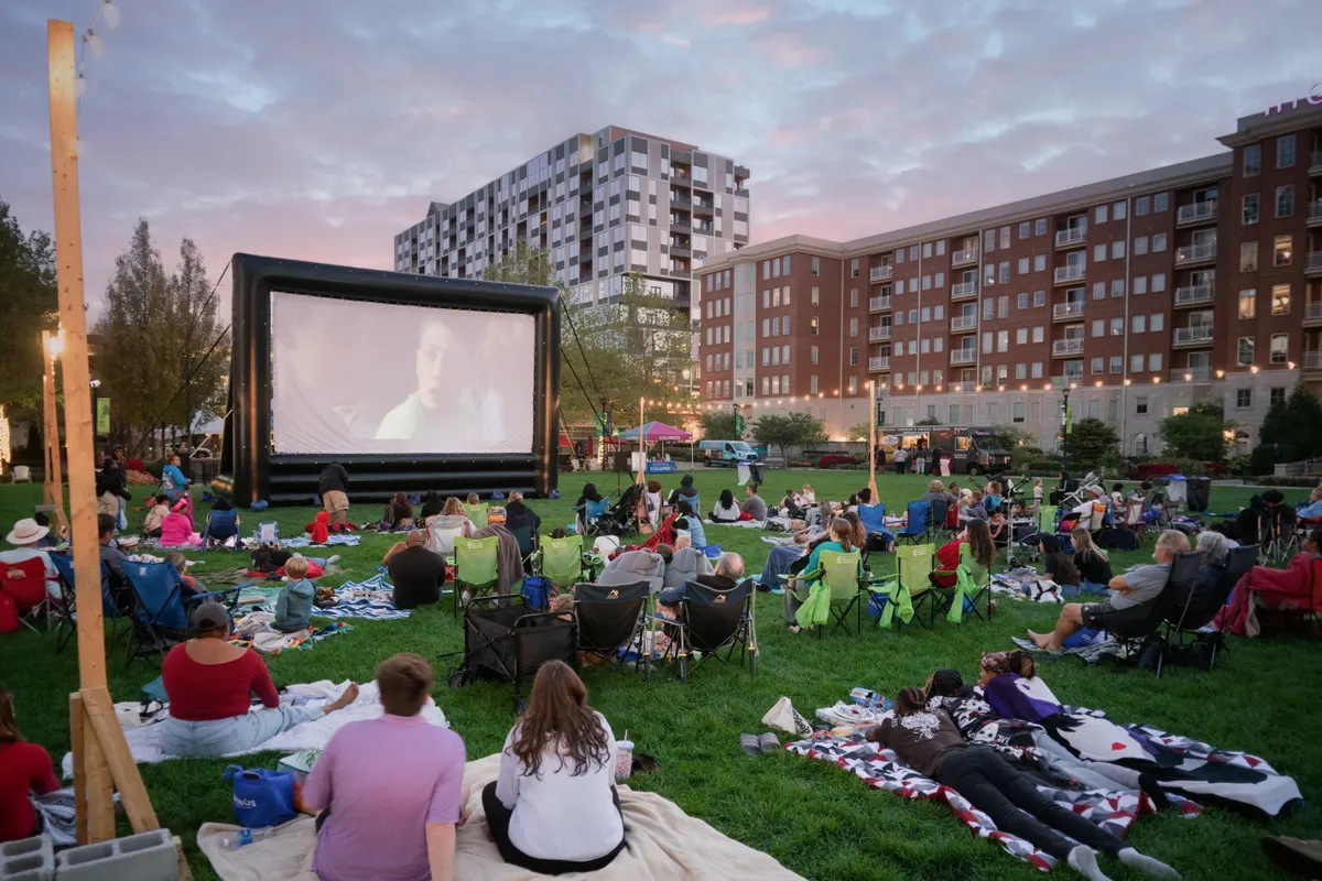 Crowd on lawn watching an outdoor movie screen at sunset