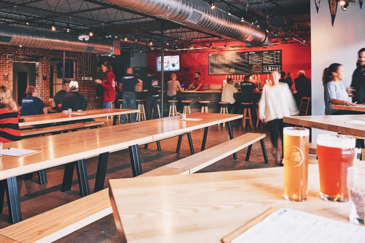 Taproom with long wood tables, bar, and two beers