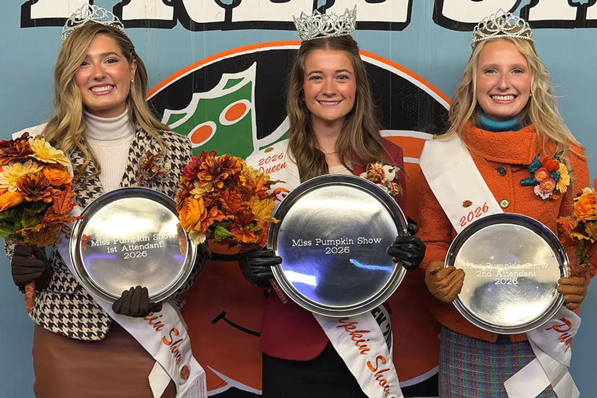 Three pumpkin show queens in tiaras and sashes hold silver trays