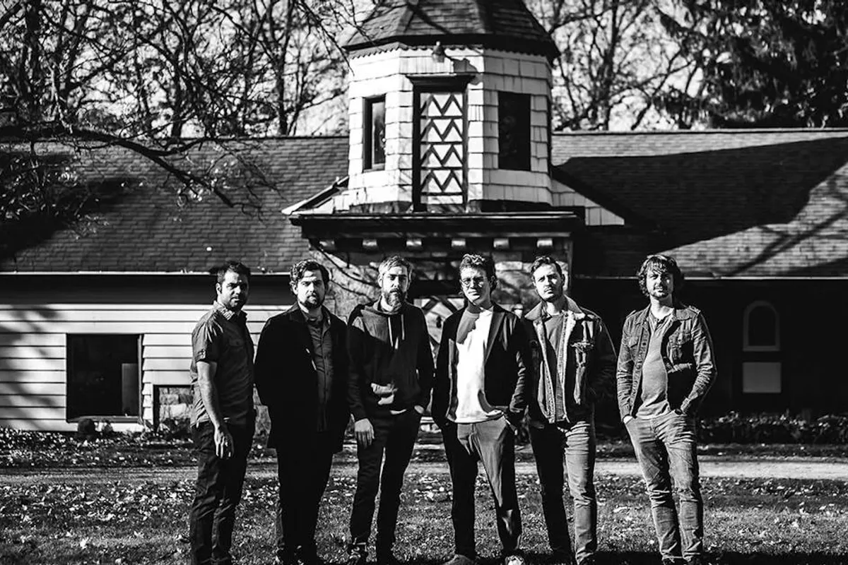 Six band members stand in front of a building, black and white