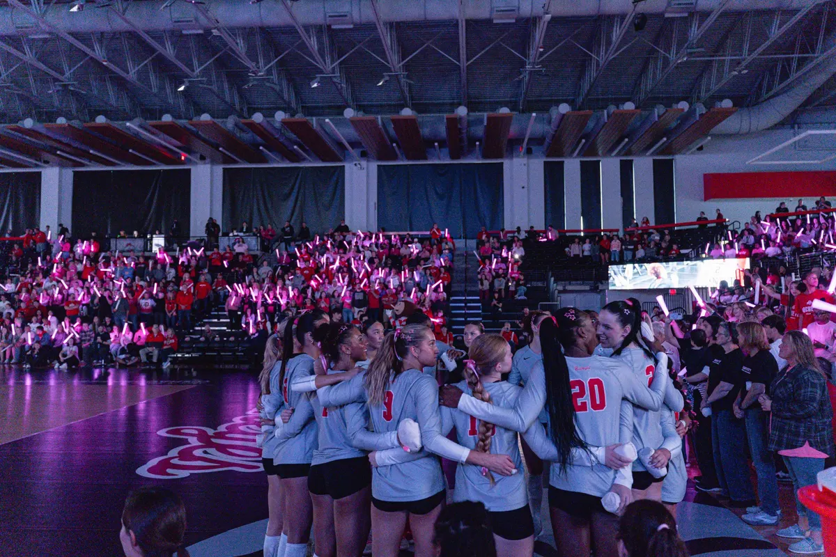 Volleyball team huddles before a crowd with glowing lights in the arena
