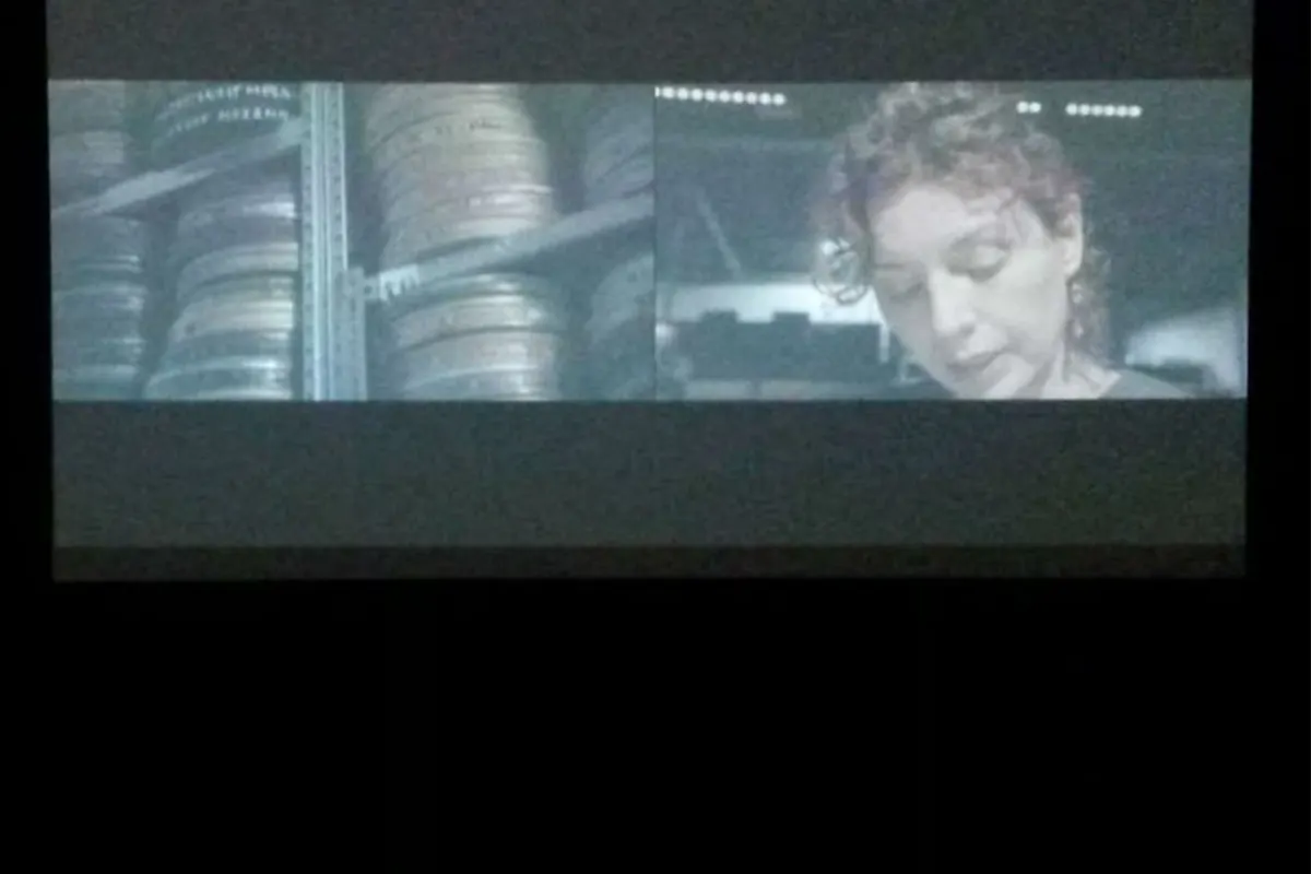 Performer at a laptop beside a screen showing film reels