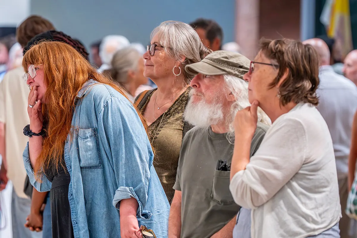 Visitors gather in a gallery, looking intently at artwork