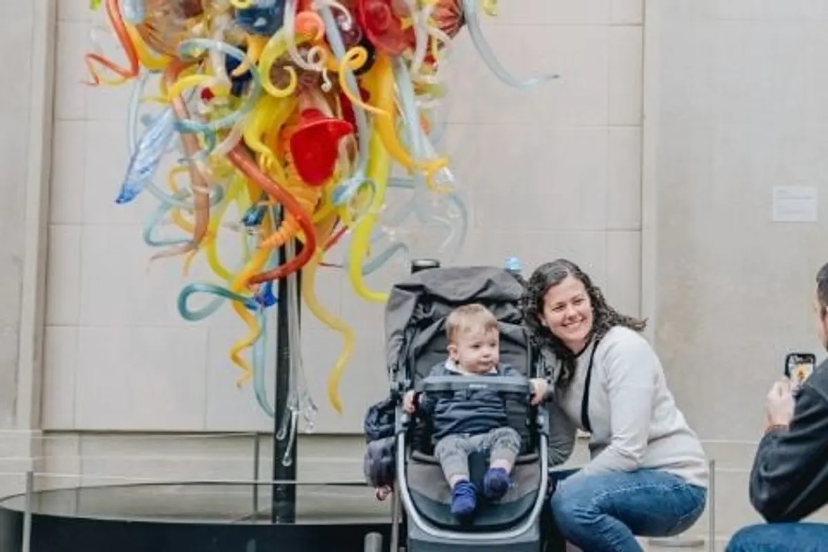 Family poses with a baby stroller beside a colorful glass chandelier sculpture