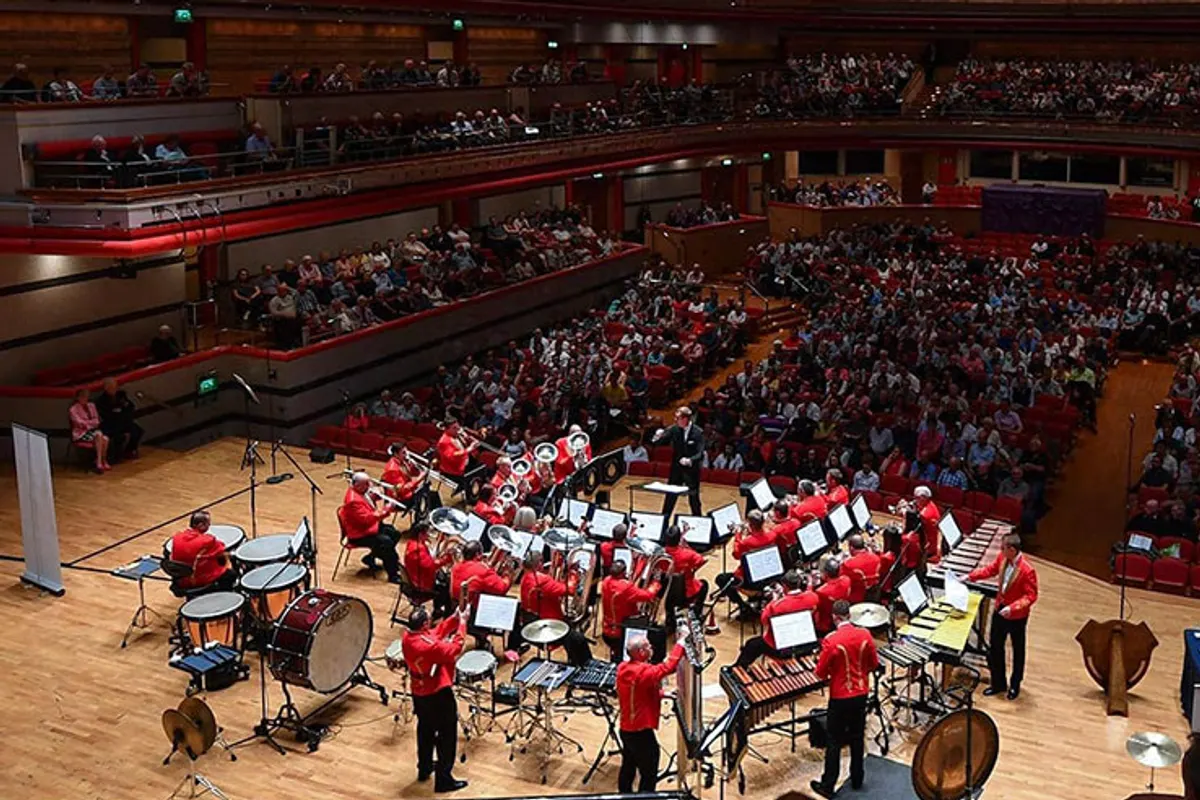 Brass band in red jackets performing on stage before a full hall